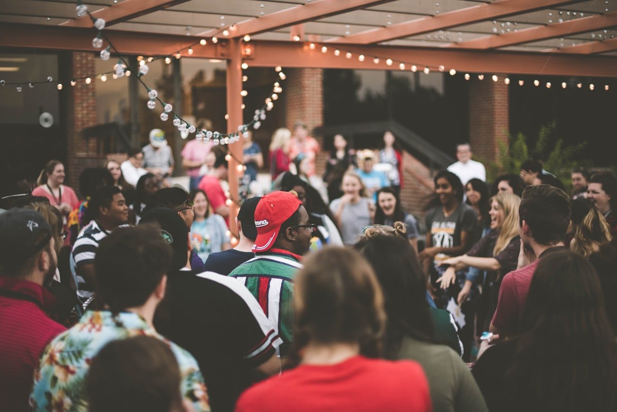People gathered outdoors at a busy public venue strung with lights
